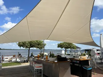 a large white umbrella over a bar with a view of the water at Apartment Oostergeest by Interhome in Uitgeest