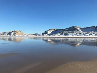 a beach with snow covered mountains in the background at Solaris in Egmond aan den Hoef