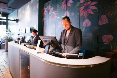 a man in a suit standing at a counter with computers at Ambassador City Centre Hotel in Haarlem