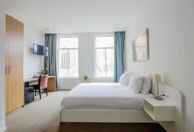 a bedroom with a white bed and a desk and window at Ambassador City Centre Hotel in Haarlem