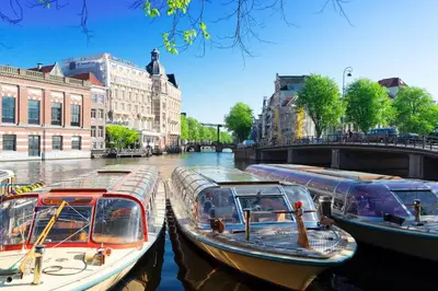 three boats are docked on a river in a city at Luxury House With 2 Private Independent Studios 120 m2 Near LEIDSEPLEIN CITY CENTRE AMSTERDAM - Paid Parking Possibilities Nearby in Amsterdam