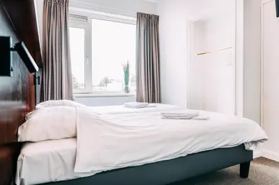 a bedroom with a bed with white sheets and a window at Hotel Café Restaurant Abina in Amstelveen