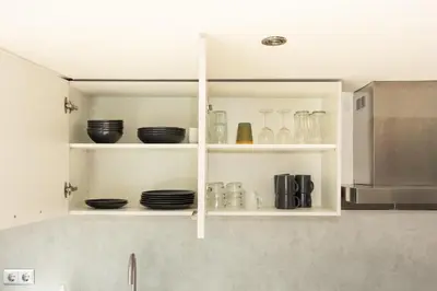 a kitchen with white cabinets with plates and bowls at Tulip Marina - garden sauna in Nieuwe-Niedorp