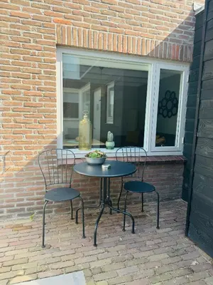 a patio with two chairs and a table and a window at Hello Katwijk - Zomerhuis Paul Krügerstraat 3 in Katwijk aan Zee