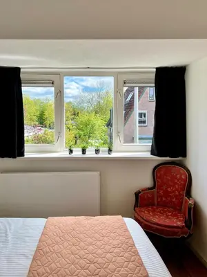 a bedroom with a bed and a chair and two windows at The Grutto, private apartment 25 min from city center in Amsterdam