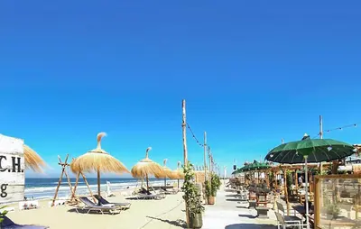 a beach with straw umbrellas and chairs and the ocean at 2 Bedroom Nice Home In Noordwijkerhout in Noordwijkerhout