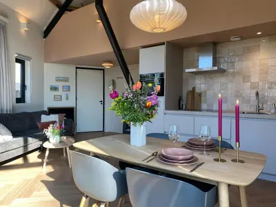 a kitchen and living room with a wooden table with pink candles at Ons Huisje Achter - De Hooischuur in Noordwijkerhout