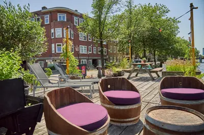 a patio with wooden chairs and tables and a building at The Amsterdam Houseboat Family - de Pijp in Amsterdam