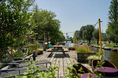 a wooden deck with a table and benches next to a river at The Amsterdam Houseboat Family - de Pijp in Amsterdam