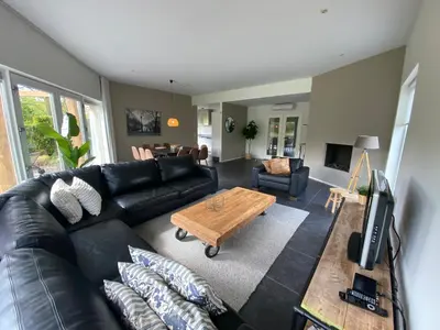 a living room with a black leather couch and a coffee table at Villa Riverside met hottub, eigen aanlegsteiger, zwemtrap, trampoline en kano's in Zeewolde