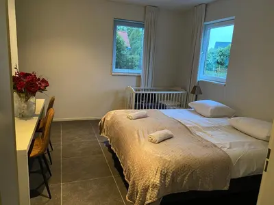 a bedroom with a bed and a desk and two windows at Villa Riverside met hottub, eigen aanlegsteiger, zwemtrap, trampoline en kano's in Zeewolde