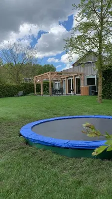 a blue trampoline in the grass in front of a house at Villa Riverside met hottub, eigen aanlegsteiger, zwemtrap, trampoline en kano's in Zeewolde