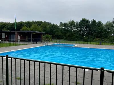 a large blue swimming pool next to a fence at Villa Riverside met hottub, eigen aanlegsteiger, zwemtrap, trampoline en kano's in Zeewolde