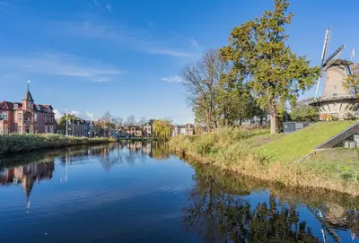 a river in a city with a windmill in the background at Molenzicht in Alkmaar
