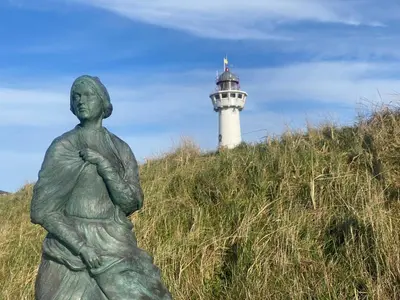 a statue of a woman with a lighthouse in the background at Studio Eb in Egmond aan Zee