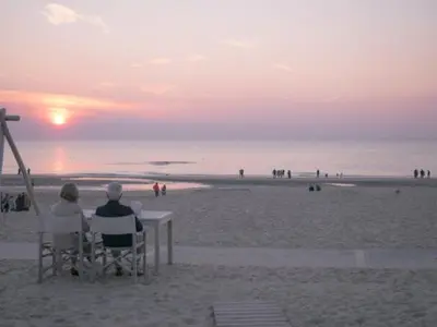 two people sitting in chairs watching the sunset at the beach at Villa aan Zee in Noordwijk