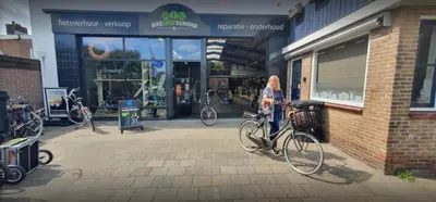 a woman standing in front of a store with her bike at Beach house met parkeerplaats in het centrum in Egmond aan Zee