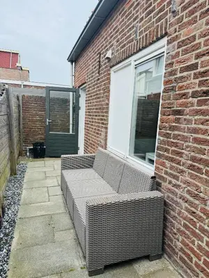 a wicker couch sitting on the side of a brick building at Hello Noordwijk - Tiny house Julianastraat 12 in Noordwijk aan Zee