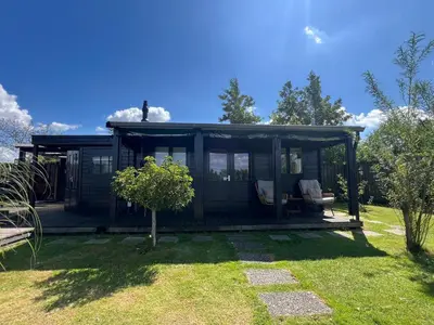 a black cabin with a deck in a yard at New- The Cabana- With Sauna and Hot Tub, on a lake near Amsterdam in Vinkeveen