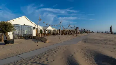 a beach with a building and flags in the sand at Beach Lodge 24 - Noordwijk aan Zee - met eigen tuin in Noordwijk