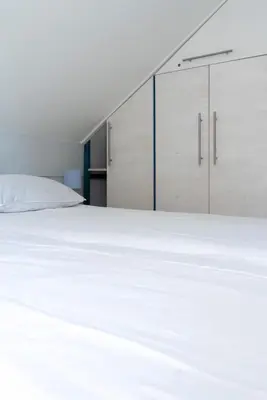 a bedroom with a white bed and white cabinets at -Duinhuisje - voor families & honden nabij strand in Noordwijk