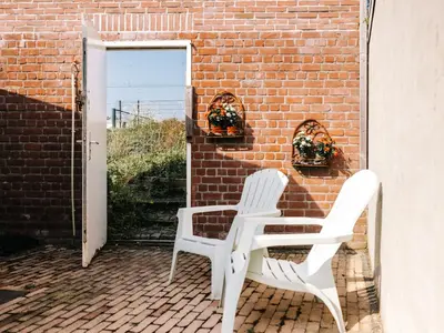 two white chairs sitting next to a brick wall at Rosa's Cottage, garden and free parking in Zandvoort