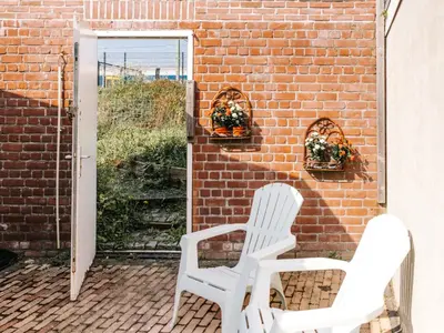 two white chairs sitting on a patio with a brick wall at Rosa's Cottage, garden and free parking in Zandvoort