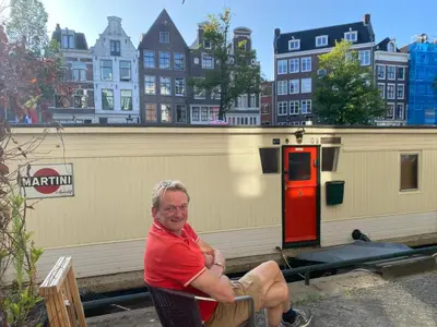 a man sitting in a chair in front of a building at Pantheos Top Houseboat in Amsterdam