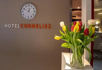 a vase of flowers on a table with a clock at Hotel Cornelisz in Amsterdam