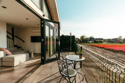 a patio with a table and chairs and flowers at Bos, duin en strand huisje in Noordwijk