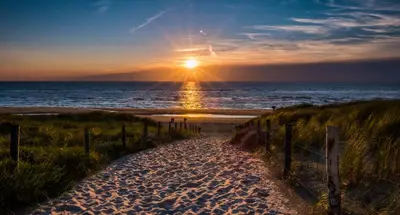 a sunset at the beach with a path to the beach at Bos, duin en strand huisje in Noordwijk