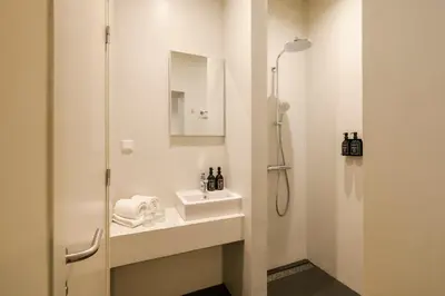 a white bathroom with a sink and a shower at Hotel Bloemendaal by BHC in Bloemendaal