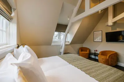 a bedroom with a white bed and two chairs at Hotel Bloemendaal by BHC in Bloemendaal