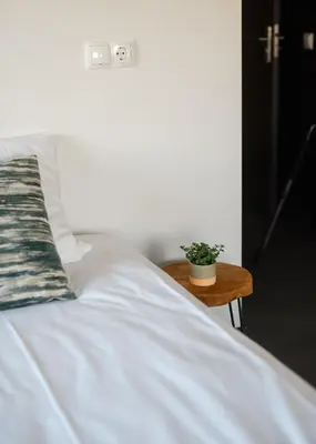 a white bed with a plant on a wooden table at B&B Hartenlust kamer de Boomgaard in Bodegraven