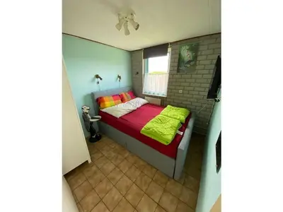 a bedroom with a bed with a red and yellow blanket at Noordzee omheind met hond in Dirkshorn
