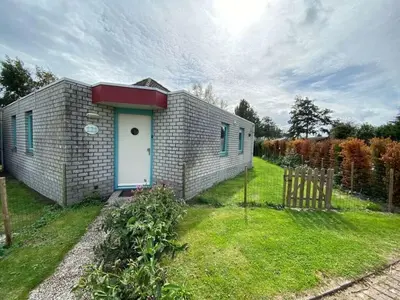 a small brick house with a door in the grass at Noordzee omheind met hond in Dirkshorn