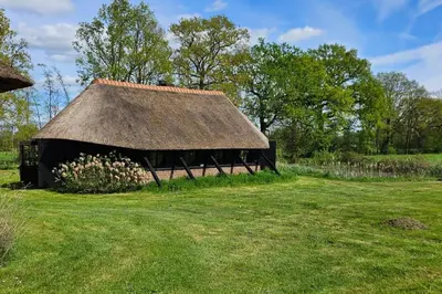 a black barn with a thatched roof in a field at Natuurhuisje op Landgoed Groot Diermen in Putten