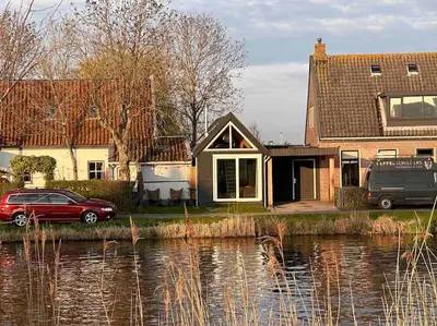 a house with a car parked next to a body of water at Tiny house of Picasso in Warmenhuizen