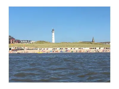 a beach with a lighthouse and a crowd of people at On the coast Comfortable holiday residence in Egmond aan Zee