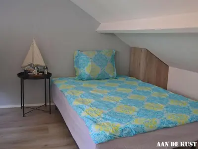 a bed with a blue and yellow comforter in a room at On the coast Comfortable holiday residence in Egmond aan Zee
