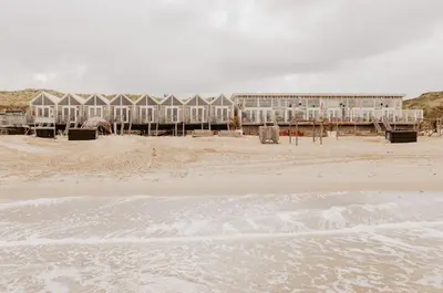 a beach with a building in the background and the ocean at Strandhuisjes Zoomers aan Zee in Castricum