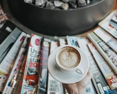 a person holding a cup of coffee on top of books at Hotel V Frederiksplein in Amsterdam