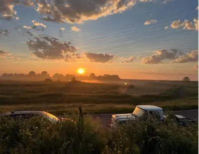 two trucks parked in a field with the sunset in the background at Casey's Lake View House Boat in Amsterdam