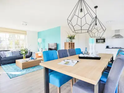 a dining room and living room with a wooden table and blue chairs at Holiday Home Tapuit 6-1 by Interhome in Noordwijk