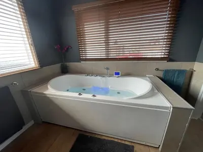 a large white tub in a bathroom with two windows at Poellodge XL, houseboat met whirlpool en sauna in Aalsmeer