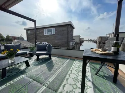 a balcony with a table and chairs and a house at Poellodge XL, houseboat met whirlpool en sauna in Aalsmeer