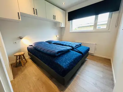 a bedroom with a bed with blue sheets and a window at Bungalowpark de Horn - Floresta 214 in Dirkshorn