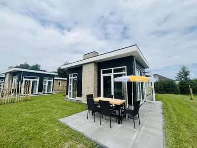 a house with a table and chairs and an umbrella at Bungalowpark de Horn - Floresta 215 in Dirkshorn
