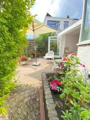 a patio with a bench and an umbrella and flowers at Tranquil Guest House in Zandvoort