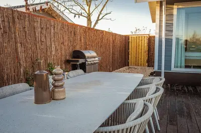 a table with chairs and a grill in a backyard at Waterfront tiny home with spacious garden in Vinkeveen